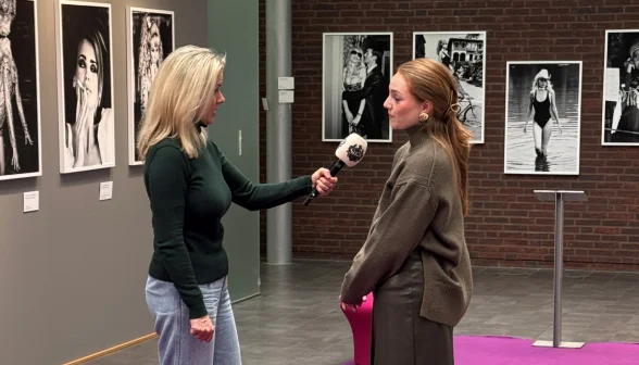 Twee vrouwen in een interview in een galerie met zwart-witfoto's aan de muur. Eén vrouw houdt een microfoon vast.