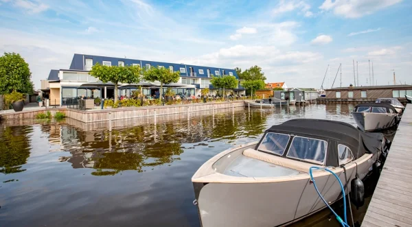 Appartementen aan het water met boten aangemeerd aan een steiger, omgeven door groen en een heldere lucht.