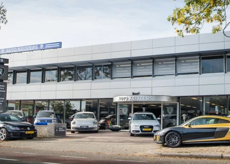 Autodealer Auto Keijzers met moderne gevel, meerdere geparkeerde auto's voor de showroom, waaronder een sportwagen.