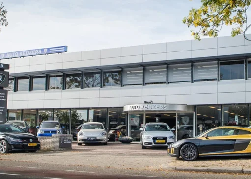 Autodealer Auto Keijzers met moderne gevel, meerdere geparkeerde auto's voor de showroom, waaronder een sportwagen.