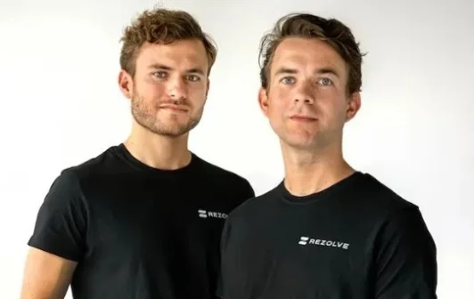 Twee mannen in zwarte shirts met het logo "Rezolve" poseren voor een witte achtergrond.