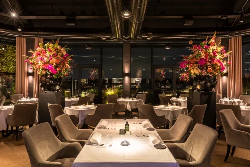 Luxe restaurantinterieur met gedekte tafels, grote bloemstukken en zachte verlichting.